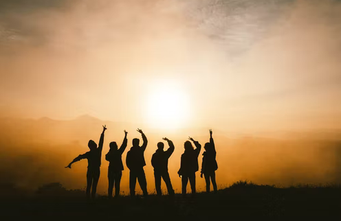A group of people raising their hands during a sunset