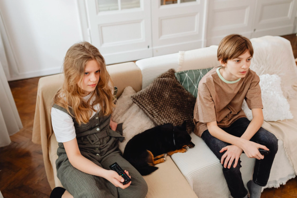 Two children sitting on a sofa watching television to learn about their family history.
