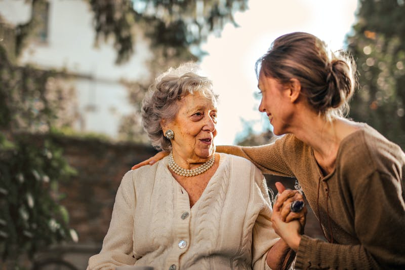 A woman sitting with her grandmother as they have a conversation.