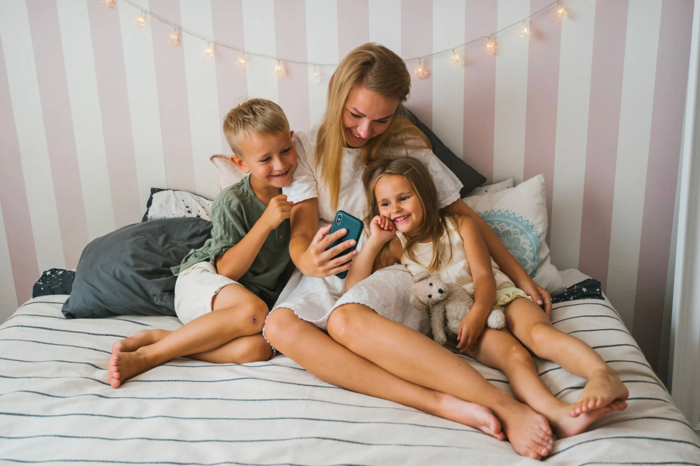 A mother cuddles with her children in bed as they speak to someone on the phone.